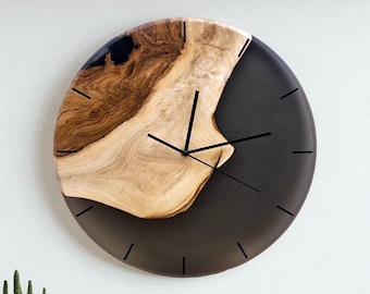 Puede incluir: Un reloj de pared redondo con un diseño de madera natural y resina gris oscuro. La esfera del reloj tiene manecillas y marcadores de hora negros. La veta de la madera es visible, añadiendo un toque rústico. Es un artículo decorativo.