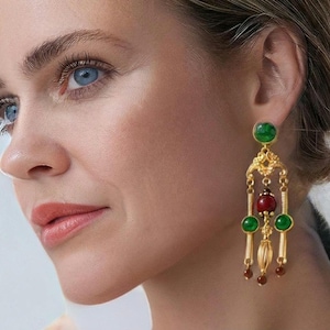 Peut inclure: Boucles d'oreilles pendantes dorées avec des pierres précieuses vertes et rouges. Les boucles d'oreilles présentent un motif de filigrane décoratif et plusieurs éléments pendants. Les pierres précieuses sont rondes et ovales, ajoutant une touche de couleur et d'élégance.
