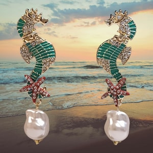 Peut inclure: Une paire de boucles d'oreilles en ton or avec un hippocampe vert et rouge avec une goutte de perle et une étoile de mer rouge.