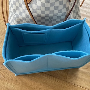 Pode incluir: Um organizador de bolsa de feltro azul claro com vários compartimentos e um bolso pequeno. O organizador é projetado para caber dentro de uma bolsa maior, como uma bolsa tote.