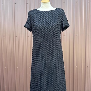 May include: A black short-sleeved dress with a textured, quilted pattern. The dress has a round neckline and a straight, A-line silhouette.