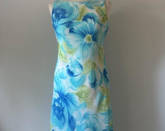 May include: A sleeveless dress with a floral pattern in blue and green on a white base. The dress has a scoop neck and a knee-length hem. The floral design features large, stylized blooms.