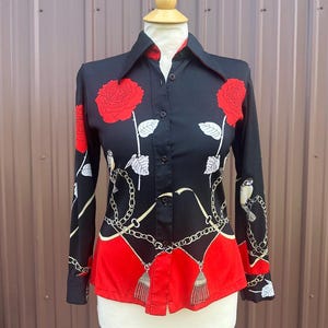 Może przedstawiać: Czarno-czerwona koszula z długim rękawem zapinana na guziki z kwiatowym nadrukiem przedstawiającym róże, liście i ptaki. Koszula ma kołnierzyk i wzór łańcucha.