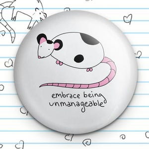 Könnte beinhalten: Weißer Knopf mit einer schwarz-weißen Cartoon-Ratte mit rosa Ohren und Schwanz. Der Text "embrace being unmanageable" steht unter der Ratte.