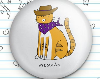 Puede incluir: Un botón blanco con una ilustración de dibujos animados de un gato atigrado naranja que lleva un sombrero de vaquero marrón y un pañuelo morado con estrellas blancas. El gato está sentado con la cola enroscada alrededor de sus patas. El texto "meowdy" está escrito debajo del gato.
