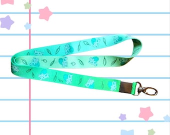 May include: A teal and green lanyard with a repeating pattern of small blue and white cartoon frogs and green leaves. The lanyard has a silver swivel clasp.