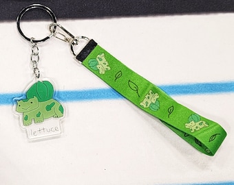 May include: A green and white keychain with a cartoon character on a clear acrylic charm. The charm says "lettuce". The keychain has a green ribbon with cartoon characters and leaves.