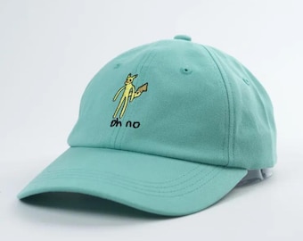 May include: A turquoise blue baseball cap with an embroidered yellow cartoon character holding a gun and the text "oh no".