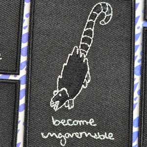 May include: Black embroidered patch with a white outline of a cartoon animal with a curled tail. The text "become ungovernable" is embroidered in white below the animal.