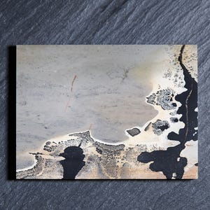 May include: A rectangular slab of polished stone featuring a smooth, light gray surface with a prominent, jagged black and cream-colored dendritic pattern along the right side, resembling a natural landscape or an abstract aerial view of a coastline.