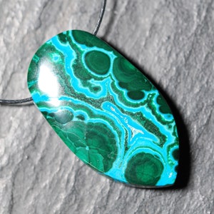 May include: A green and blue gemstone pendant with a swirling pattern. The pendant is attached to a black cord.