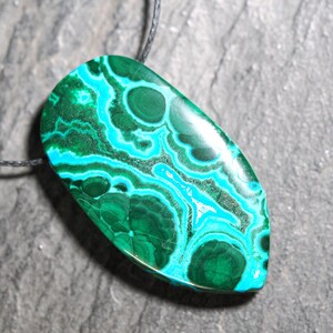 May include: A green and blue malachite pendant with a swirling pattern, hanging from a black cord.