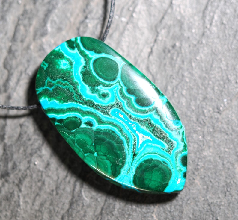 May include: A green and blue malachite pendant with a swirling pattern, hanging from a black cord.