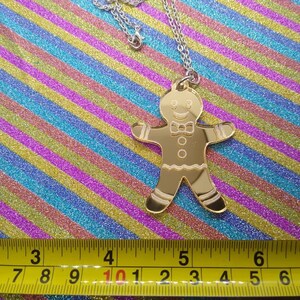 May include: Gold-colored gingerbread man pendant necklace. The pendant is about 4 inches tall and is on a silver chain.