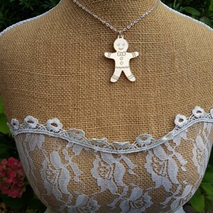 May include: A silver chain necklace with a gingerbread man pendant. The pendant is made of metal and has a white finish. The gingerbread man is smiling and has a bow tie.