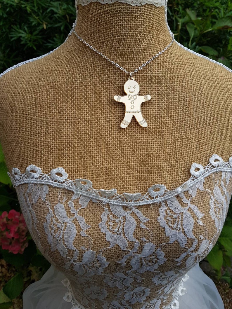 May include: A silver chain necklace with a gingerbread man pendant. The pendant is made of metal and has a white finish. The gingerbread man is smiling and has a bow tie.
