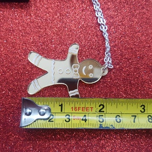 May include: Gold gingerbread man charm necklace with a silver chain. The charm is about 2 inches tall and 1.5 inches wide.