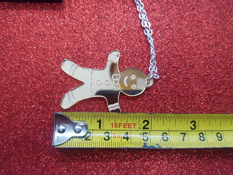 May include: Gold gingerbread man charm necklace with a silver chain. The charm is about 2 inches tall and 1.5 inches wide.
