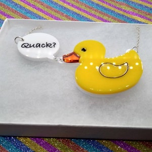 May include: A yellow rubber duck necklace with a white speech bubble charm that says "Quack?"