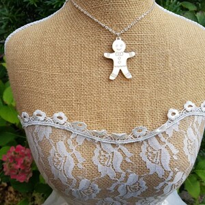 May include: A silver necklace with a gingerbread man pendant. The pendant is a simple outline of a gingerbread man with a smile and buttons.