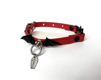 May include: Red leather pet collar with a black bat charm and a silver coffin pendant.