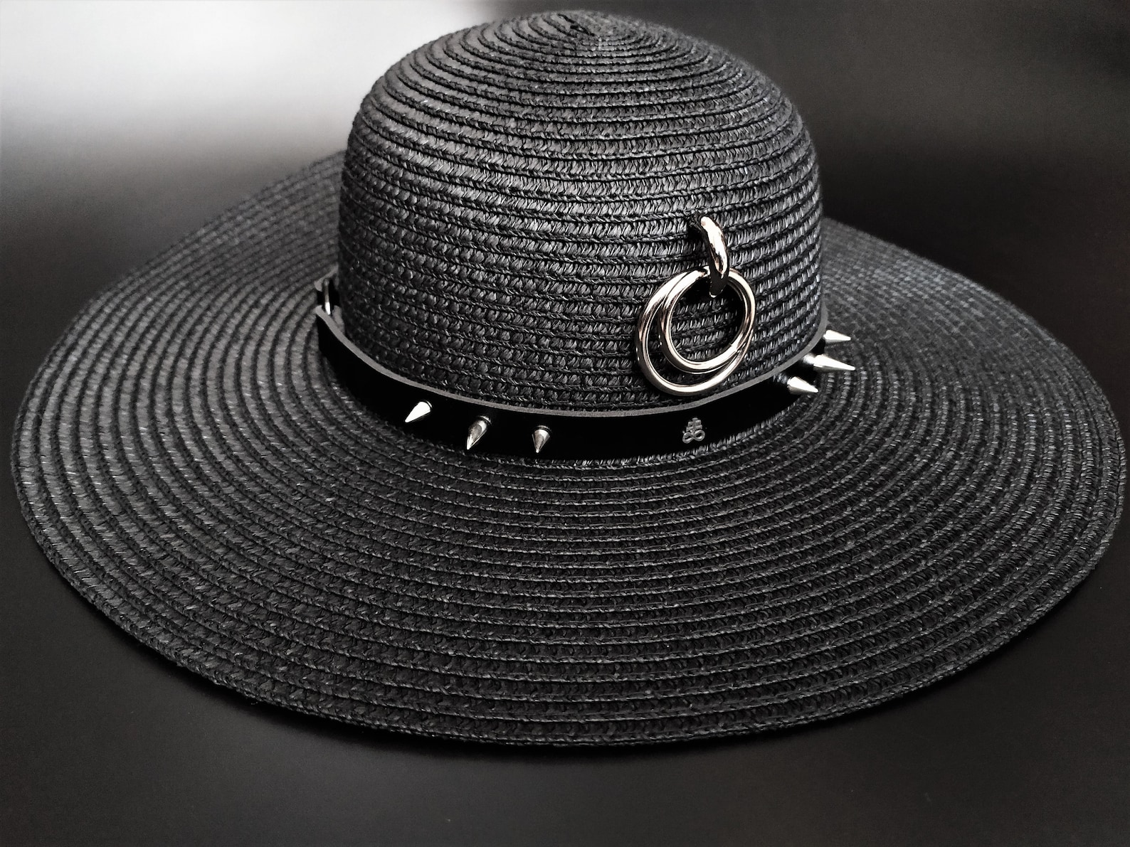 Black wide-brim sun hat with silver spikes and O-ring detail, bold accessory for edgy summer goth or punk-inspired beach style.