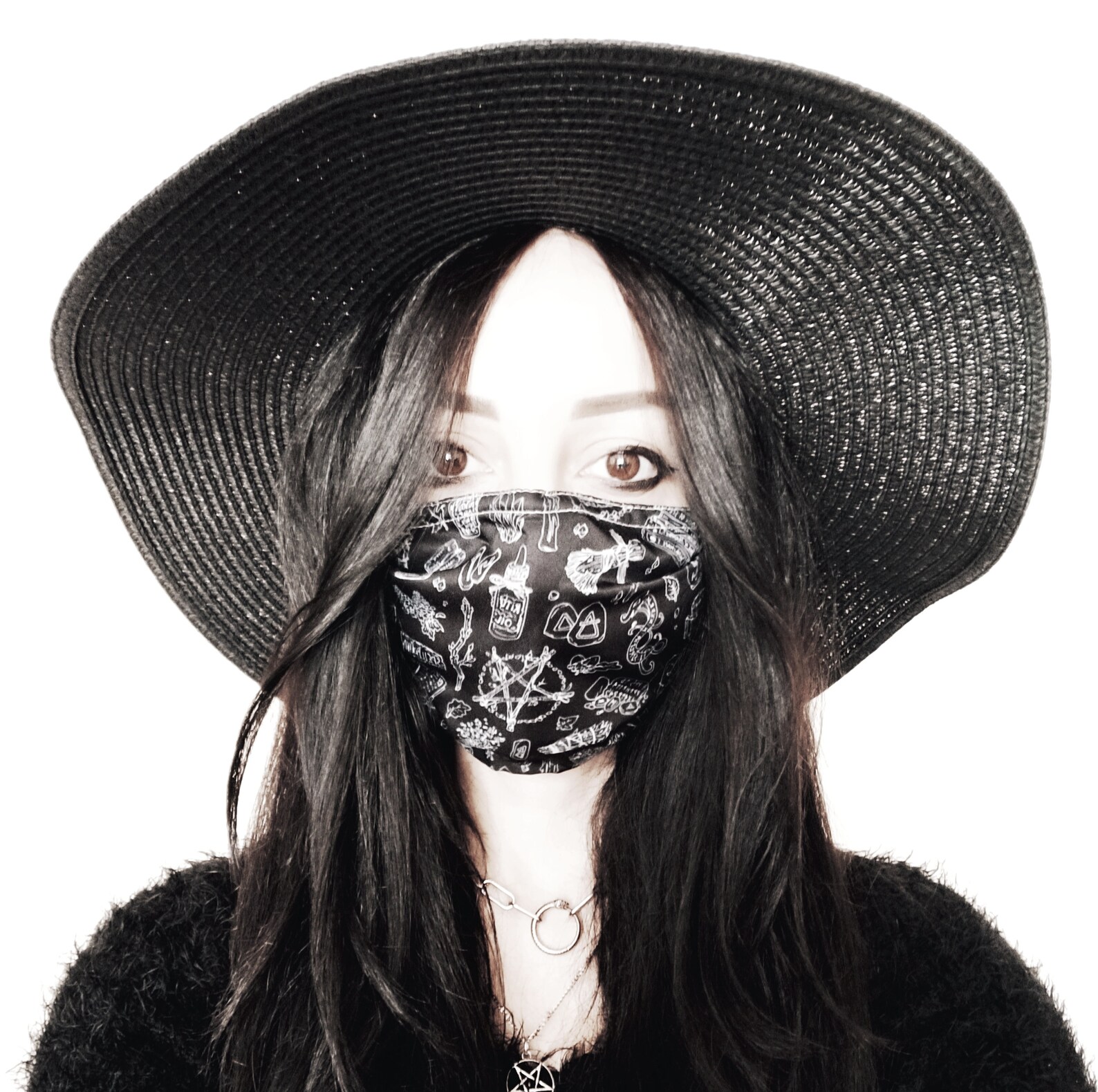 Goth woman in wide-brim black sun hat and occult print face mask, showcasing a mysterious and stylish look.