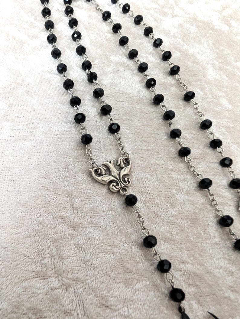 May include: A black beaded rosary necklace with a silver ornate pendant. The beads are faceted and the chain is silver.