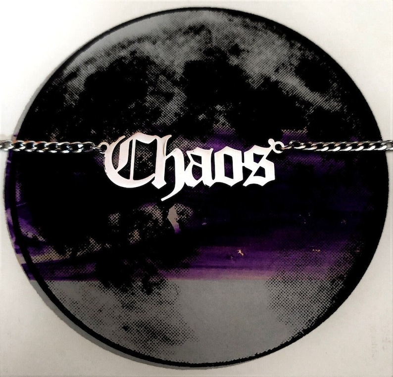 May include: A silver necklace with a gothic-style pendant that reads "Chaos". The pendant is on a black and purple background.
