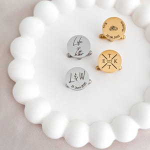 Gravierte Edelstahl-Manschettenknöpfe mit Initialen und Symbolen auf Dekoteller – personalisiertes Geschenk für Hochzeit und Trauzeugen.