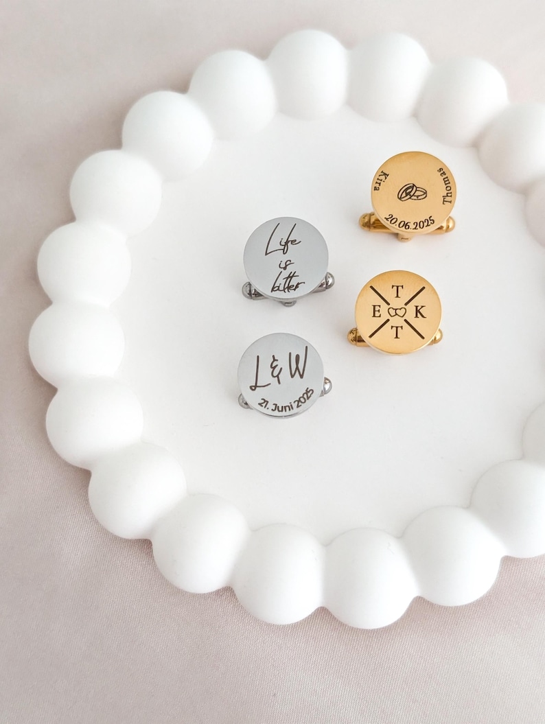 Gravierte Edelstahl-Manschettenknöpfe mit Initialen und Symbolen auf Dekoteller – personalisiertes Geschenk für Hochzeit und Trauzeugen.