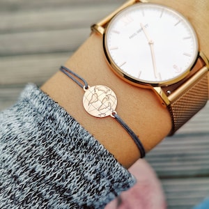 Tragefoto Armband Weltkarte mit einer roségoldenen Weltkarte und grauem Band. Am Handgelenk eine roségoldene Uhr