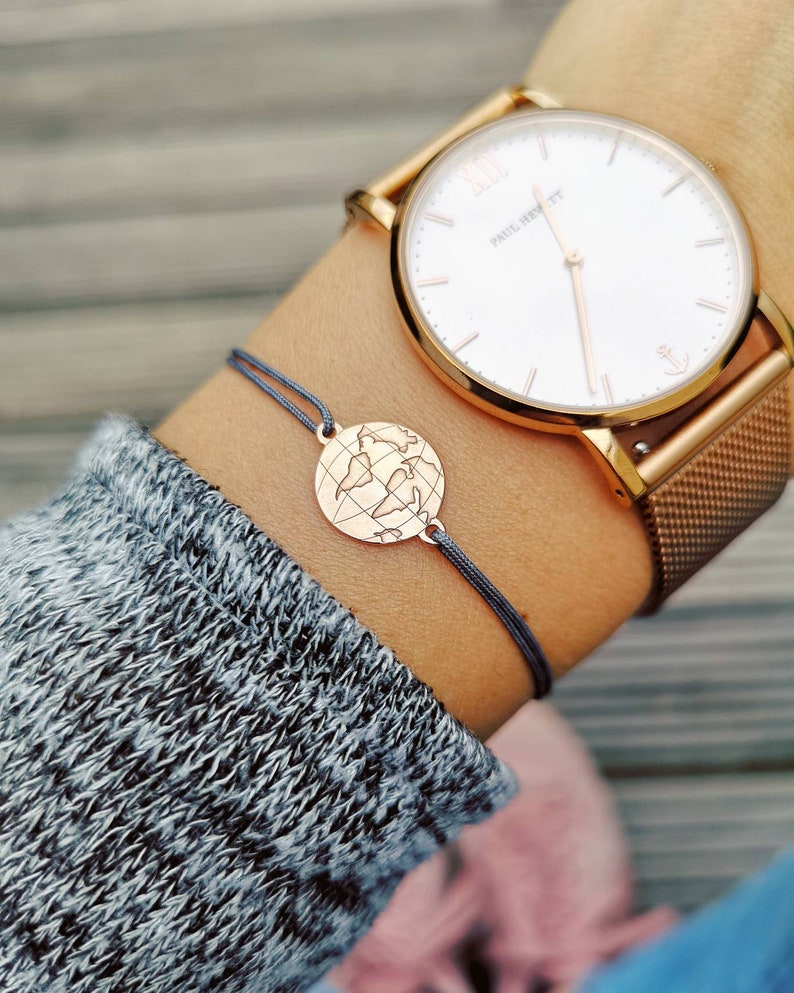 Tragefoto Armband Weltkarte mit einer roségoldenen Weltkarte und grauem Band. Am Handgelenk eine roségoldene Uhr