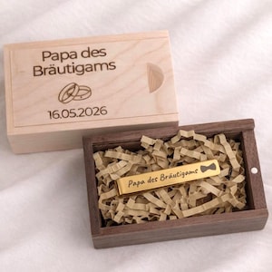 Könnte beinhalten: Eine Holzkiste mit dem Text "Papa des Bräutigams" und dem Datum "16.05.2026" auf dem Deckel graviert. Im Inneren befindet sich eine kleinere Holzkiste mit einer goldfarbenen Krawattenklammer mit demselben Text.