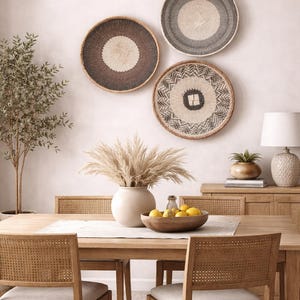 May include: A dining room scene featuring a wooden table and chairs, adorned with decorative woven wall baskets. A vase of pampas grass and a wooden bowl of lemons add to the decor. A lamp and a small tree are also visible.