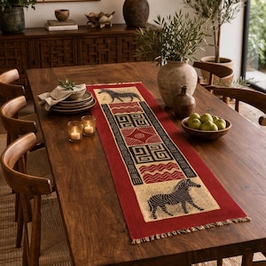 May include: A wooden dining table set with a red table runner featuring black zebra and geometric patterns. The table is set with plates, candles, and a bowl of green pears. The room has a warm, inviting atmosphere.
