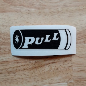 May include: Black and white sticker of a bullet with the word "PULL" printed on it.