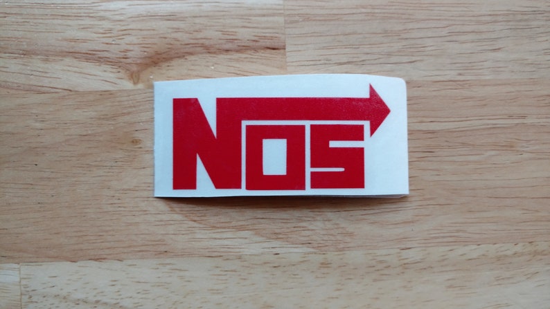 May include: Red "NOS" sticker with an arrow pointing to the right. The sticker is on a light brown wooden surface.