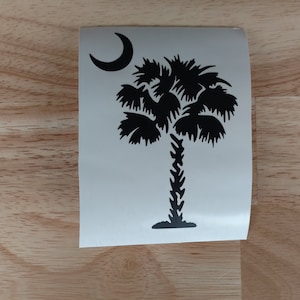 May include: A black and white vinyl decal of the South Carolina state flag, featuring a palmetto tree and a crescent moon.