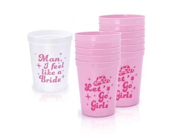 May include: Set of pink and white plastic cups with a bachelorette party theme. The pink cups have a cowboy hat graphic and the text "Let's Go Girls". The white cup has the text "Man, I feel like a Bride".
