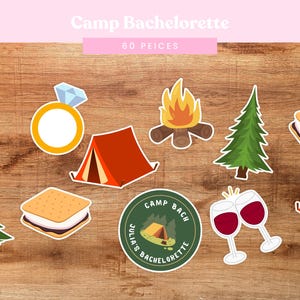 May include: A set of 60 printable party props for a bachelorette party with a camping theme. The props include a tent, a campfire, a s'more, a wine glass, a ring, a pine tree, and a circle with the text "Julia's Camp Bach Bachelorette".