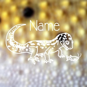 May include: White outline illustration of a gecko with the word "Name" above it and a small insect. The gecko has a spotted pattern and is facing right. The background is a blurred mix of yellow and white.