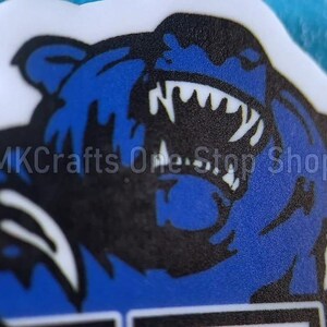 May include: A blue and black bear with a fierce expression, its mouth open and teeth bared. The bear is on a white background.