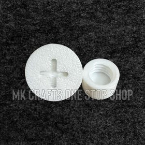 May include: Two white plastic components. One is a circular cap with a cross-shaped indentation. The other is a cylindrical piece with internal threading. The text "MK CRAFTS ONE STOP SHOP" is visible.