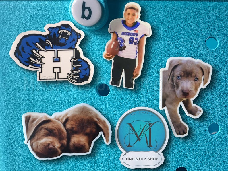 May include: A blue background with five stickers. The stickers are of a blue bear with claws, a football player wearing a white jersey with the number 83, a gray puppy, two brown puppies sleeping, and a blue circle with the letter M and the text "One Stop Shop".
