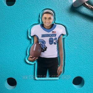 May include: A clear acrylic charm featuring a young person in a football uniform, holding a football. The uniform is white with blue accents and the word "Bearcats" and the number "83". The charm is on a turquoise background. The text "MK CRAFTS ONE STOP SHOP" is at the bottom.