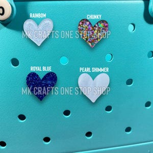 Pu&ograve; includere: Quattro ciondoli a forma di cuore in vari colori e trame. I ciondoli sono etichettati come "Rainbow", "Chunky", "Royal Blue" e "Pearl Shimmer". Ogni ciondolo ha il testo "MK CRAFTS ONE STOP SHOP" sotto. Lo sfondo &egrave; di colore azzurro.