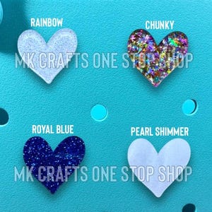 Pu&ograve; includere: Quattro ciondoli a forma di cuore in vari colori: azzurro, glitter chunky multicolore, blu reale e perla scintillante. I testi "RAINBOW", "CHUNKY", "ROYAL BLUE" e "PEARL SHIMMER" sono sopra ogni cuore. Il testo "MK CRAFTS ONE STOP SHOP" &egrave; sotto.