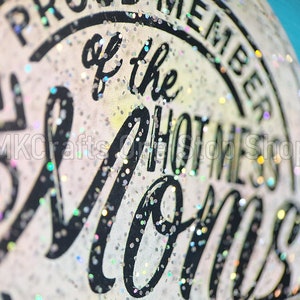K&ouml;nnte beinhalten: Nahaufnahme eines wei&szlig;en, glitzernden Aufklebers mit schwarzem Text, der "Proud Member of the Hottest Moms" lautet.