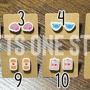 Puede incluir: Doce pares de pendientes coloridos con varios diseños relacionados con el ámbito médico. Los diseños incluyen un estetoscopio, un gorro de enfermera, un cerebro, una mascarilla facial, pulmones, un corazón, vendas, un portapapeles, un frasco de pastillas y una pastilla. Los pendientes están numerados del 1 al 12.